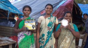 A woman entrepreneur and her customers holding solar lanterns in urban Indian slum.